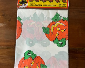 May include: A plastic Halloween tablecloth featuring a repeating pattern of orange jack-o'-lanterns with green leaves. The tablecloth measures 52" x 72" (132 x 183cm) and has a header with the words "Halloween Tablecloth".