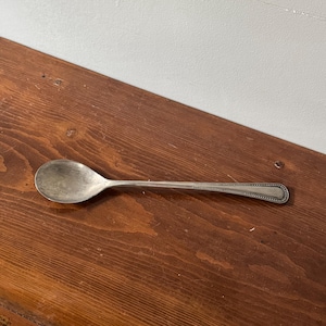 Puede incluir: Una cuchara de plata con un cuenco redondeado y un mango largo y delgado. El mango tiene un patrón decorativo de pequeños puntos.