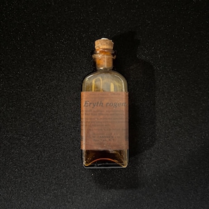 Könnte beinhalten: Kleine, antike Glasflasche mit Korken. Die Flasche hat ein braunes Papieretikett mit dem Text "Eryth rogers" und anderem unleserlichen Text. Die Flasche ist mit einer gelben Flüssigkeit gefüllt. Die Flasche ist wahrscheinlich ein Vintage-Apothekenartikel.