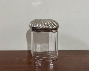 Tarro de tocador vintage con tapa plateada y forma ovalada.