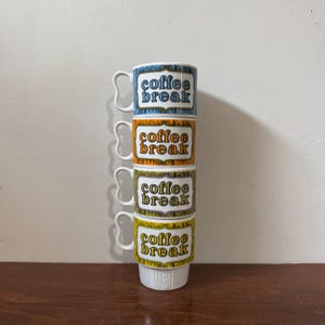 May include: Four stacked vintage coffee mugs, each with the words "coffee break" in orange and white. The mugs have blue, orange, green, and yellow borders. The mugs have a distinctive handle design. The mugs are stacked on top of each other.