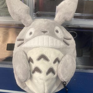 Op de afbeelding: Een pluche, grijze Totoro-ge&iuml;nspireerde karakter met grote oren, een brede grijns en donkergrijze markeringen. Het karakter heeft een witte buik met donkergrijze pijlvormige markeringen. Een zwarte clip is aan de onderkant bevestigd.