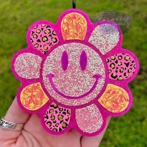 May include: Pink glitter flower shaped charm with a smiley face in the center. The flower has a swirl pattern, leopard print, and glitter accents.