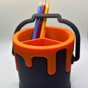 May include: Orange paint can shaped desk organizer with three compartments and a black handle.  Three colored pencils are in the organizer.