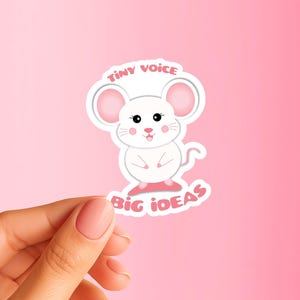 May include: A white mouse sticker with pink accents, featuring the text "TINY VOICE BIG IDEAS". The cartoon mouse has large pink ears, black eyes, and a smiling face. The sticker is held against a pink background.