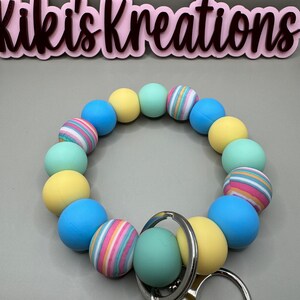 May include: A colorful silicone beaded keychain with a silver key ring. The beads are yellow, blue, and green with some striped patterns. The keychain is a great way to add a pop of color to your keys.