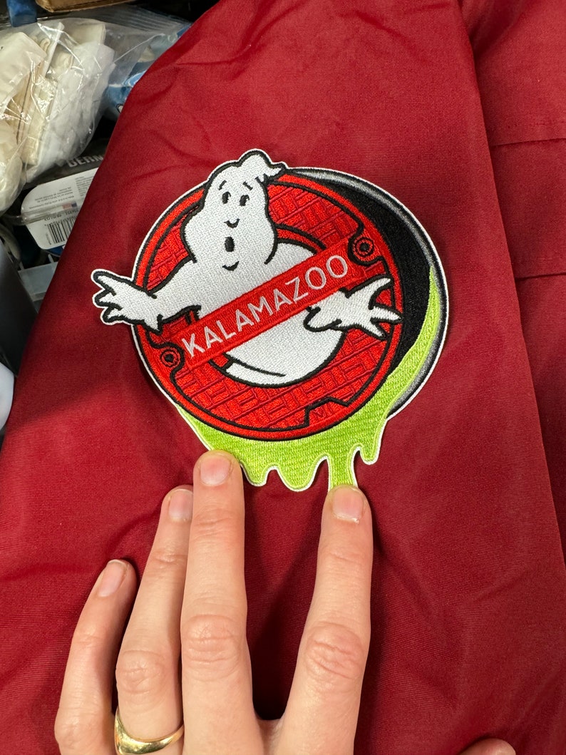 Peut inclure: Une veste rouge avec un &eacute;cusson brod&eacute; vert, blanc et noir repr&eacute;sentant un fant&ocirc;me et le texte "KALAMAZOO".