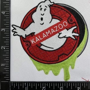 Peut inclure: Un patch brod&eacute; rouge et blanc avec une figure de fant&ocirc;me et le texte "KALAMAZOO" dans une banni&egrave;re rouge. Le fant&ocirc;me est entour&eacute; d'une bordure verte en forme de slime.