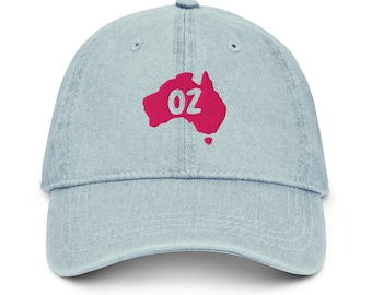 Op de afbeelding: Lichtblauwe denim baseballcap met een roze geborduurde kaart van Australië en de letters "OZ". De cap heeft een gebogen klep en een verstelbare band. Het ontwerp is een knipoog naar Australië.