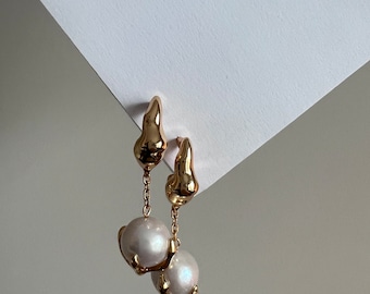 May include: A pair of gold drop earrings with a pearlescent white pearl dangling from each. The earrings have a unique, organic shape.
