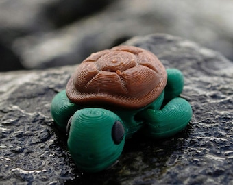 May include: A small, detailed turtle figurine with a brown shell and green body. The turtle's shell has a textured, layered design, and its head and limbs are a vibrant green. The figurine is resting on a dark, textured surface.