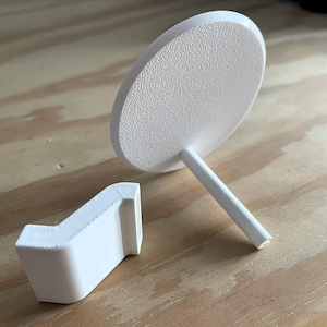 Peut inclure: Deux supports à gâteau en plastique blanc, l'un avec une base ronde et une tige haute et fine, l'autre avec une base rectangulaire incurvée.