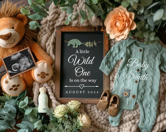 Peut inclure: Une pancarte en ardoise avec le texte "A little Wild One is on the way AUGUST 2024" entourée d'un lion en peluche, une grenouillère pour bébé, une bouteille, des fleurs et de la verdure.