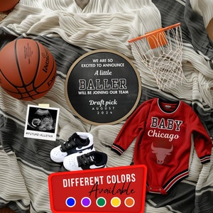 Puede incluir: Un letrero de pizarra con el texto "We are so excited to announce a little baller will be joining our team. Draft pick August 2024."  Un mameluco rojo para bebé con el texto "Baby Chicago" y un logotipo de toro. Un balón de baloncesto, un aro de baloncesto y una imagen de ultrasonido de bebé.