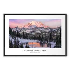 Op de afbeelding: Een panoramische foto van Mount Rainier National Park in de staat Washington. De berg is bedekt met sneeuw en de lucht is een levendige roze en oranje. Een klein meer reflecteert de kleuren van de lucht.