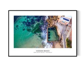 May include: An aerial view of Coogee Beach in New South Wales, Australia. The photo shows a turquoise ocean with waves crashing on the shore. A rock pool with clear blue water is visible in the foreground, along with a building with a red roof and a solar panel.