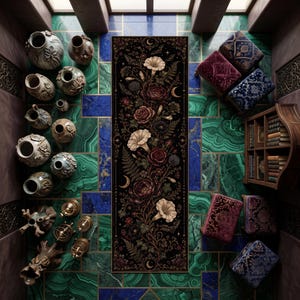 May include: A long, rectangular black runner rug featuring a detailed botanical illustration of white and dark red flowers, ferns, and crescent moons. The rug is surrounded by various ceramic vases, small stools with patterned fabric, and a wooden bookshelf.