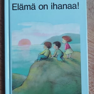 Pode incluir: Uma capa de livro azul claro com o título "Elämä on ihanaa!" em texto preto. A capa do livro apresenta uma ilustração de três crianças sentadas em uma colina verde com vista para um corpo de água com um pôr do sol rosa ao fundo. A capa do livro também inclui os nomes dos autores "Marie-Agnès Gautrat" e "Ulises Wensell" e o editor "Lasten Keskus".