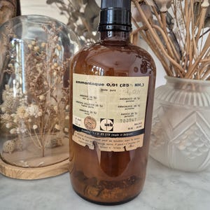 Puede incluir: Una botella de vidrio ámbar vintage con tapa de rosca negra, que presenta una etiqueta de papel desgastada impresa con 'ammoniaque 0,91 (25% NH3)' y la marca 'ucb'. La etiqueta incluye un símbolo de calavera y texto en francés e inglés.