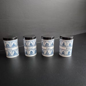 Peut inclure: Quatre pots à épices cylindriques avec des couvercles noirs et un motif nautique bleu et blanc. Les pots sont étiquetés "Laurier", "Estragon", "Thym" et "Poivre".