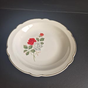 May include: Off-white, scalloped-edge serving platter with a gold rim. The platter features a floral design of red and white roses with green leaves. A classic piece for serving food or as a decorative item.