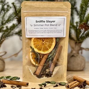 May include: A brown paper pouch with a clear window, containing a simmer pot blend called "Sniffle Slayer". The blend includes dried orange slices, cinnamon sticks, cloves, star anise, and rosemary. The pouch has a white label with the product name and ingredients.