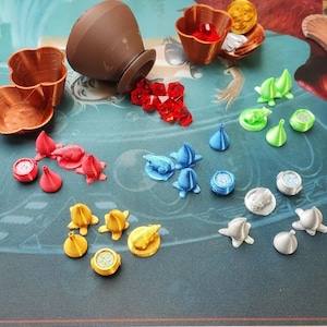 May include: A collection of colourful 3D printed game pieces, including a brown pot, red, blue, green, and silver cones, and a variety of other shapes. The pieces are arranged on a blue and green surface.