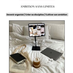 Puede incluir: Una cama blanca con un portátil, una tableta en un soporte, un cuaderno negro, una bolsa de mano y un vaso de café helado. El texto de la imagen dice "E-BOOK", "AMBITION SANS LIMITES", "Devenir organisé / Créer sa discipline / Cultiver son ambition", "Par Reine LANDA" y "AMBITION SANS LIMITES".