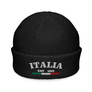 Op de afbeelding: Zwarte gebreide beanie met het woord "ITALIA" geborduurd in wit met de Italiaanse vlag en "EST 1861" eronder.