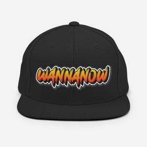 Op de afbeelding: Zwarte baseballcap met de tekst "WANNANOW" in een oranje en gele gradiënt, omlijnd met wit. De cap heeft een platte klep en een gestructureerde kroon, geschikt voor casual wear.