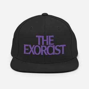 Op de afbeelding: Zwarte baseballpet met een paars geborduurd logo met de tekst "THE EXORCIST".