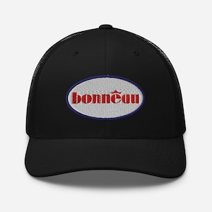Könnte beinhalten: Schwarze Trucker-Cap mit Mesh-Rückseite und gebogenem Schirm. Auf der Vorderseite befindet sich ein gesticktes ovales Patch mit dem roten Wort "Bonneau" in einer stilisierten Schrift, blau umrandet und vor weißem Hintergrund.