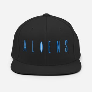 May include: A black and blue baseball cap with the word "ALIENS" embroidered in blue on the front.