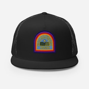 May include: Black trucker hat with a colourful patch. The patch features the text "USCSS NOSTROMO" above a mountain and star design, and the number "180286" below. The hat has a mesh back and a curved brim.