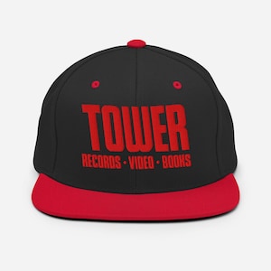 May include: Black and red snapback hat with the word "TOWER" in red block letters. Below the word "TOWER" are the words "RECORDS • VIDEO • BOOKS" in red. The hat has a red brim and a red button on top.