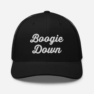以下が含まれることがあります： 白い筆記体で「Boogie Down」の刺繍が入った黒いトラッカーハット。メッシュの背面とカーブしたつばが特徴で、クラシックでカジュアルなスタイルを提供します。普段使いに最適です。