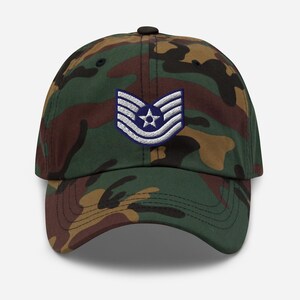 Peut inclure: Casquette de baseball camouflage avec un écusson militaire. La casquette présente un design classique à six panneaux avec une visière incurvée. L'écusson est un emblème bleu et blanc avec une étoile et des rayures. La casquette est en tissu résistant et possède une sangle réglable.