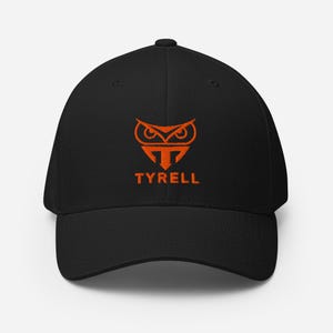 May include: Black baseball cap featuring an orange owl logo and the name "TYRELL". The cap has a curved peak and a structured fit, suitable for casual wear.