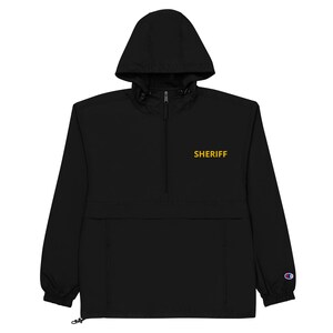 May include: Black hooded anorak jacket with a zipper closure and a gold embroidered "SHERIFF" text on the front.