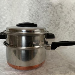 May include: A stainless steel steamer pot with a copper bottom and a black handle. The pot has a lid and a second steamer basket.