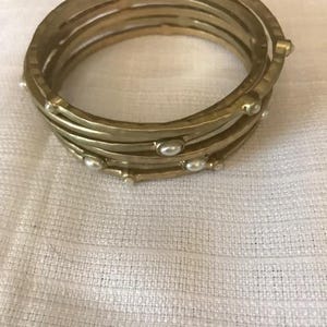 May include: A set of five gold bangles with a hammered finish and white pearl accents.