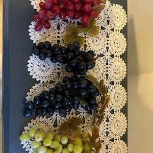 May include: Three bunches of artificial grapes on a white crocheted doily. The grapes are red, black, and green.