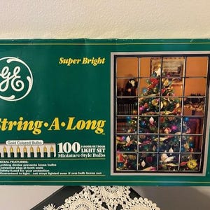 May include: A green box of GE String-A-Long miniature-style Christmas lights. The box features a picture of a decorated Christmas tree. The box reads "Super Bright" and includes a graphic of 100 gold-colored bulbs.