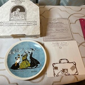 May include: A decorative plate with a blue border and a painting of three women in front of a church. The plate is labeled "When in Rome." The plate is in its original box with a guarantee of quality.