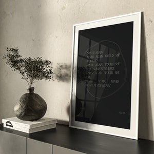 May include: A black and white framed print with a white background and black text. The text reads "NEVER AGAIN NEVER AGAIN WOULD SHE BE WEAK NEVER AGAIN WOULD SHE BEAF SOMEONE'S MERCY. NEVER AGAIN WOULD SHE FAIL. NEVER AGAIN NEVER AGAIN." The text is in a circular shape with a black background. The print is on a black surface with a vase and books in front of it.