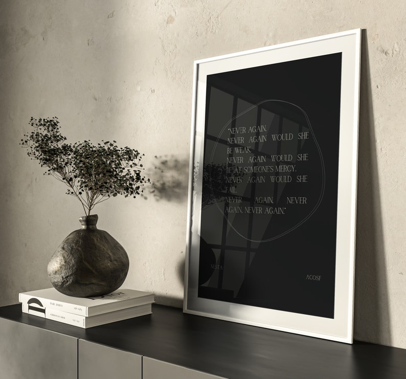 May include: A black and white framed print with a white background and black text. The text reads "NEVER AGAIN NEVER AGAIN WOULD SHE BE WEAK NEVER AGAIN WOULD SHE BEAF SOMEONE'S MERCY. NEVER AGAIN WOULD SHE FAIL. NEVER AGAIN NEVER AGAIN." The text is in a circular shape with a black background. The print is on a black surface with a vase and books in front of it.