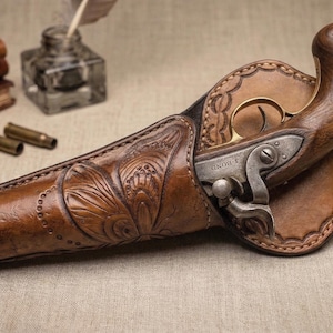 May include: A vintage pistol with a wooden handle and metal components is holstered in a brown leather case. The holster features intricate floral tooling. Several spent bullet casings and a stack of leather-bound books are in the background.