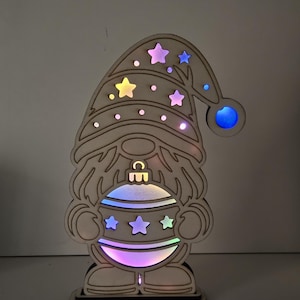 以下が含まれることがあります： 星型の切り抜きがある高い帽子と、中央に球体を持った、明るい色の木製ノームの切り抜き。デザインは背後からマルチカラーのLEDライトで照らされており、星型や円形の開口部から光が漏れ出しています。