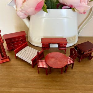 May include: Miniature red wooden dollhouse furniture set. Includes a grandfather clock, dresser, bed, desk, table, and chairs. The bed has a striped mattress, and the chairs have red and white checkered seats.