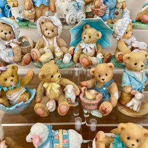 May include: A collection of detailed teddy bear figurines, each with unique outfits and accessories. Some bears hold baskets, umbrellas, or small animals. The color palette includes soft browns, blues, and whites, creating a charming and collectible aesthetic.